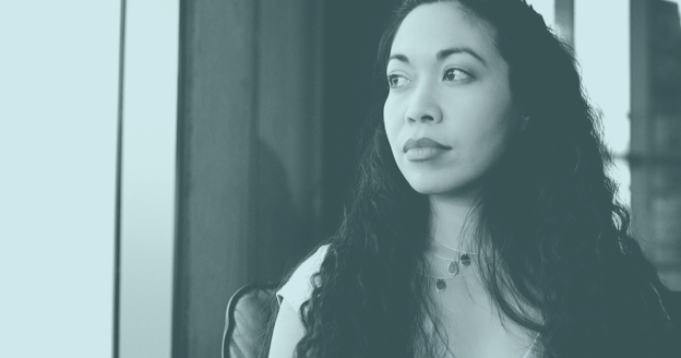 Monochromatic portrait of a woman with long curly hair gazing thoughtfully out a window, bathed in soft light.